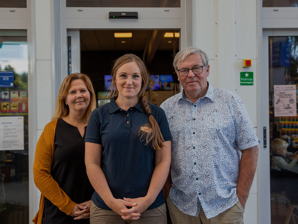 En kvinnlig stationschef tillsammans med två medlemsombud framför entren till en OKQ8 station